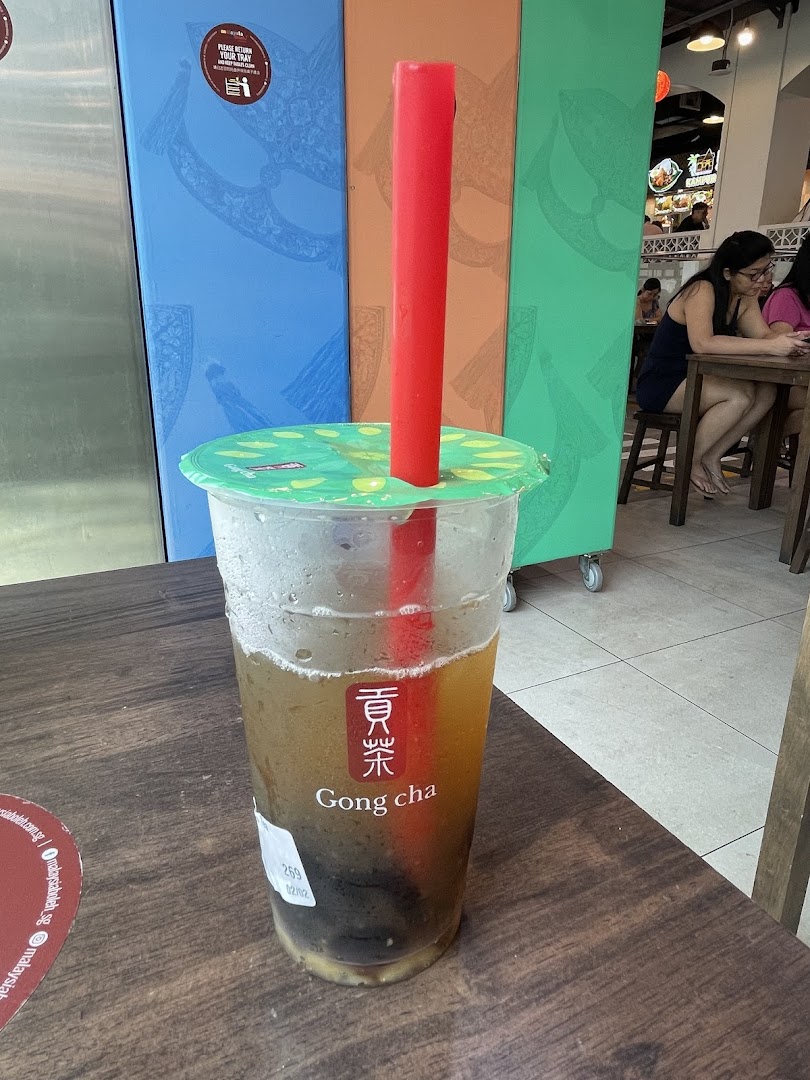 A refreshing Gong Cha bubble tea drink with a red straw on a wooden table inside the shop.