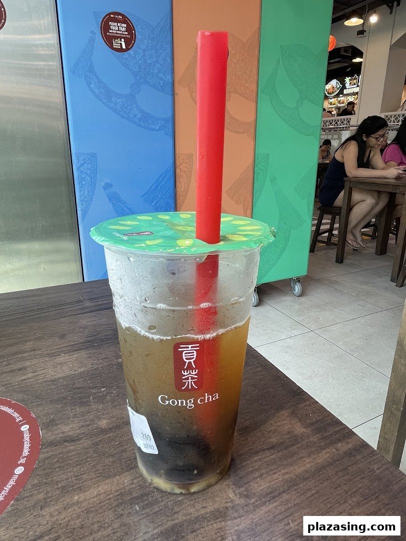 A refreshing Gong Cha bubble tea drink with a red straw on a wooden table inside the shop.