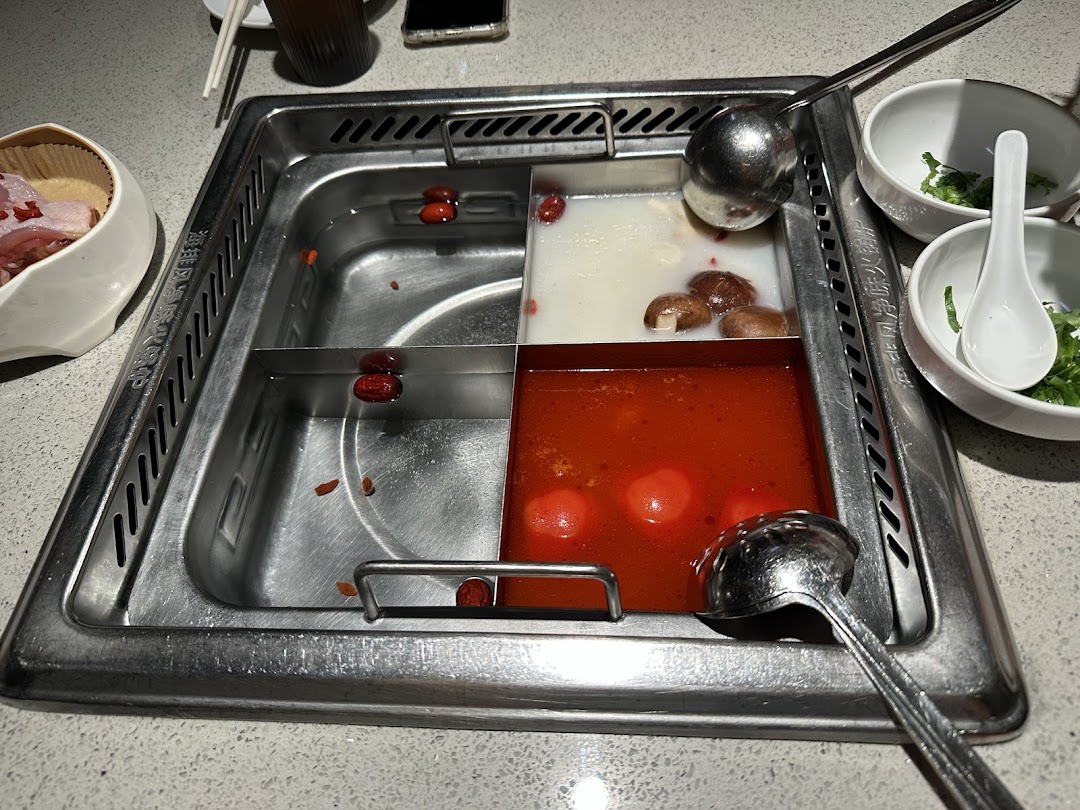 A close-up of a multi-compartment hot pot with various broths and ingredients at Haidilao.