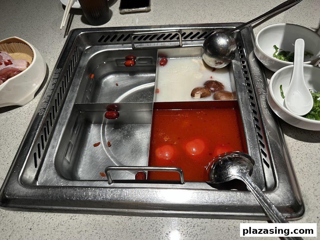 A close-up of a multi-compartment hot pot with various broths and ingredients at Haidilao.