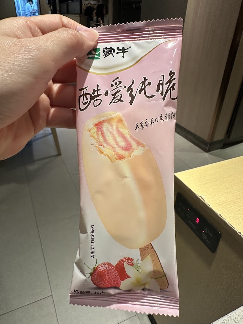 A hand holds a pink packaged strawberry vanilla ice cream bar from Mengniu.