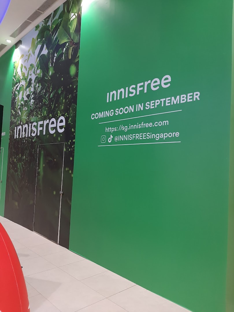 Green hoarding announcing Innisfree's upcoming opening in September, with website and social media details.