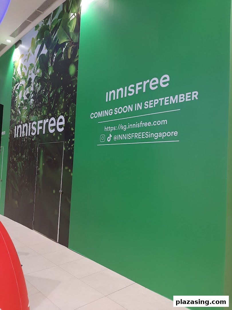 Green hoarding announcing Innisfree's upcoming opening in September, with website and social media details.