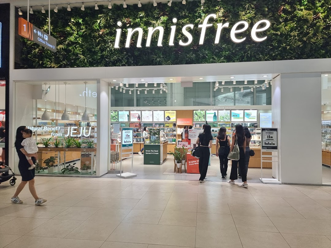 The innisfree shop entrance featuring a lush green wall with the brand logo and customers entering.