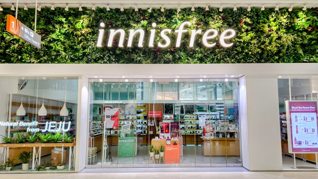 The innisfree shop front features a lush green wall with its logo, showcasing natural beauty products inside.