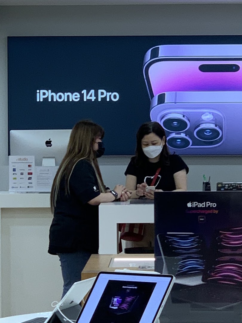 Two staff members at a counter in iStudio, with an iPhone 14 Pro display in the background.