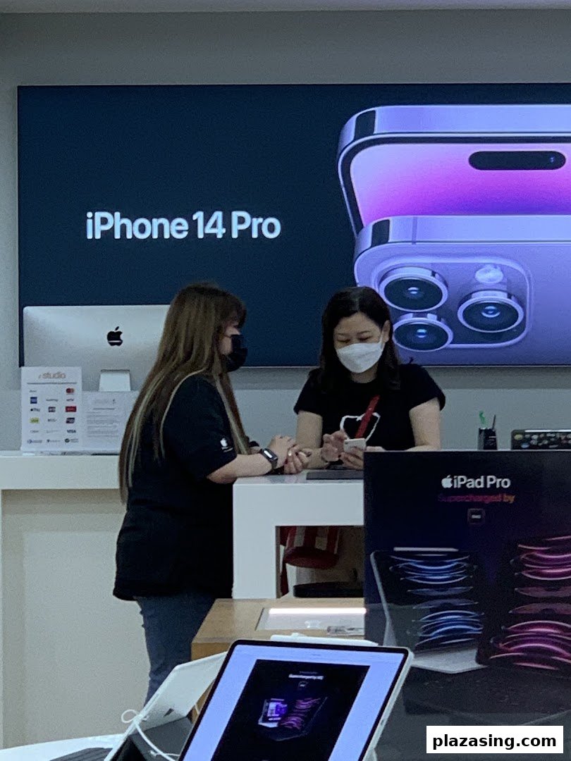 Two staff members at a counter in iStudio, with an iPhone 14 Pro display in the background.