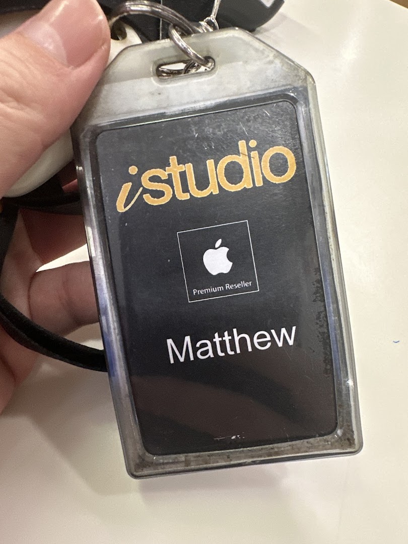 A hand holds an iStudio staff ID badge with 'Matthew' and 'Apple Premium Reseller' visible.