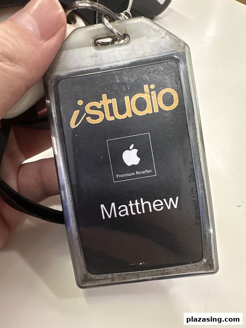 A hand holds an iStudio staff ID badge with 'Matthew' and 'Apple Premium Reseller' visible.