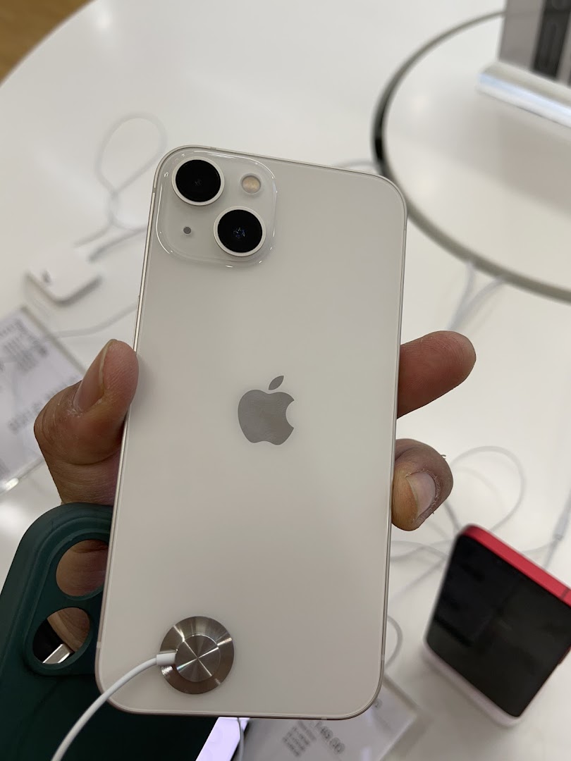 A hand holds a white iPhone 13 display model in an iStudio store.