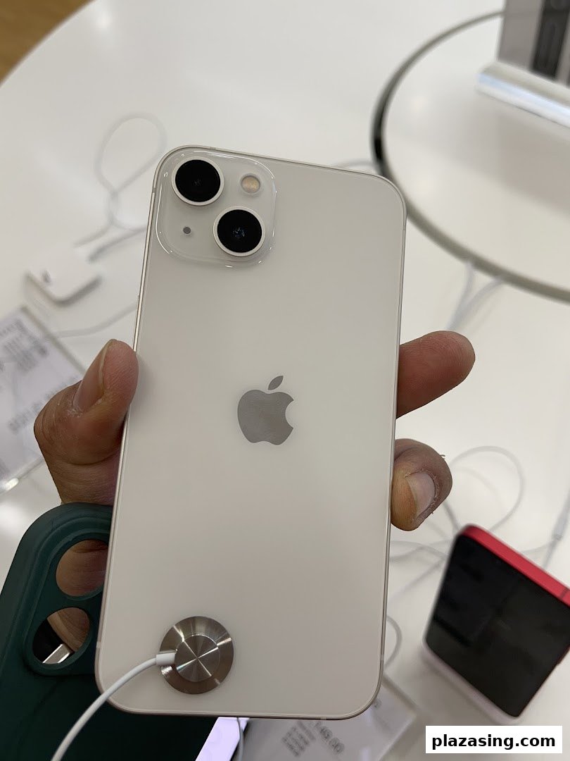 A hand holds a white iPhone 13 display model in an iStudio store.