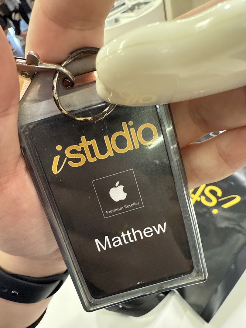 Close-up of an iStudio Apple Premium Reseller keychain/ID tag held by a hand.