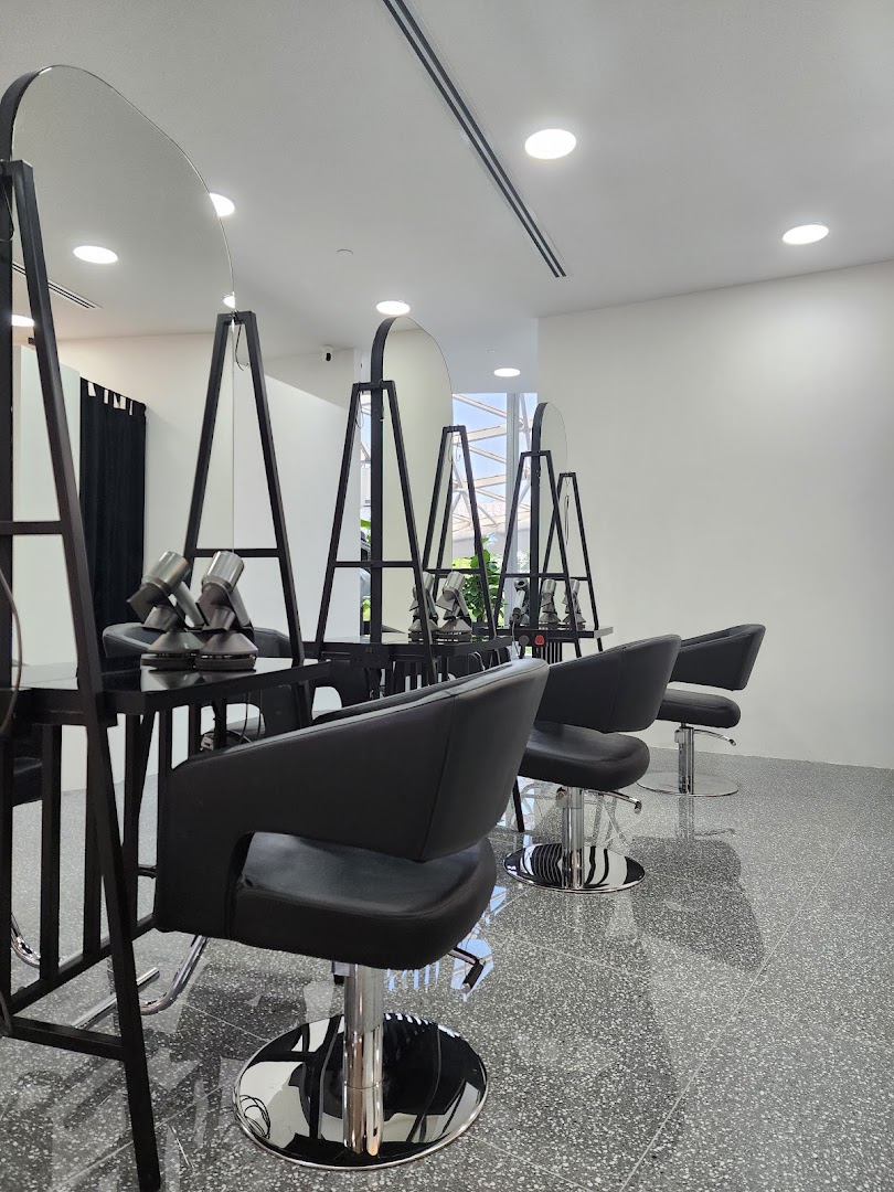A modern hair salon interior featuring multiple styling stations with black chairs and large mirrors.