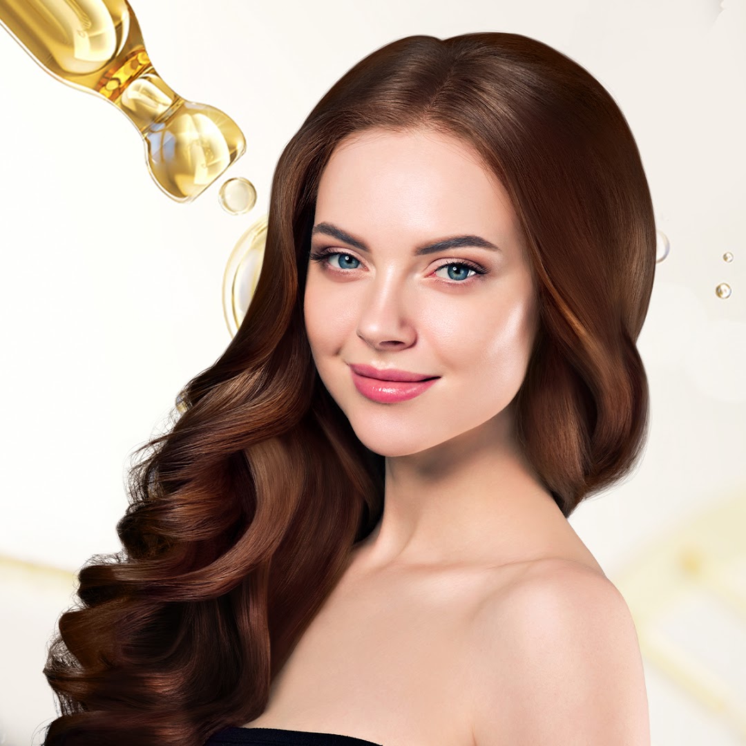 A smiling woman with long, healthy brown hair, with a dropper applying hair oil.