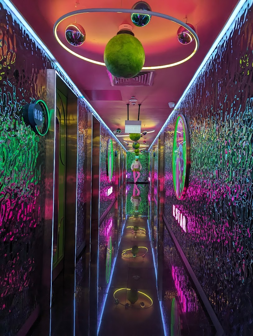 A vibrant, neon-lit hallway with reflective walls and unique decor leading to KTV rooms.