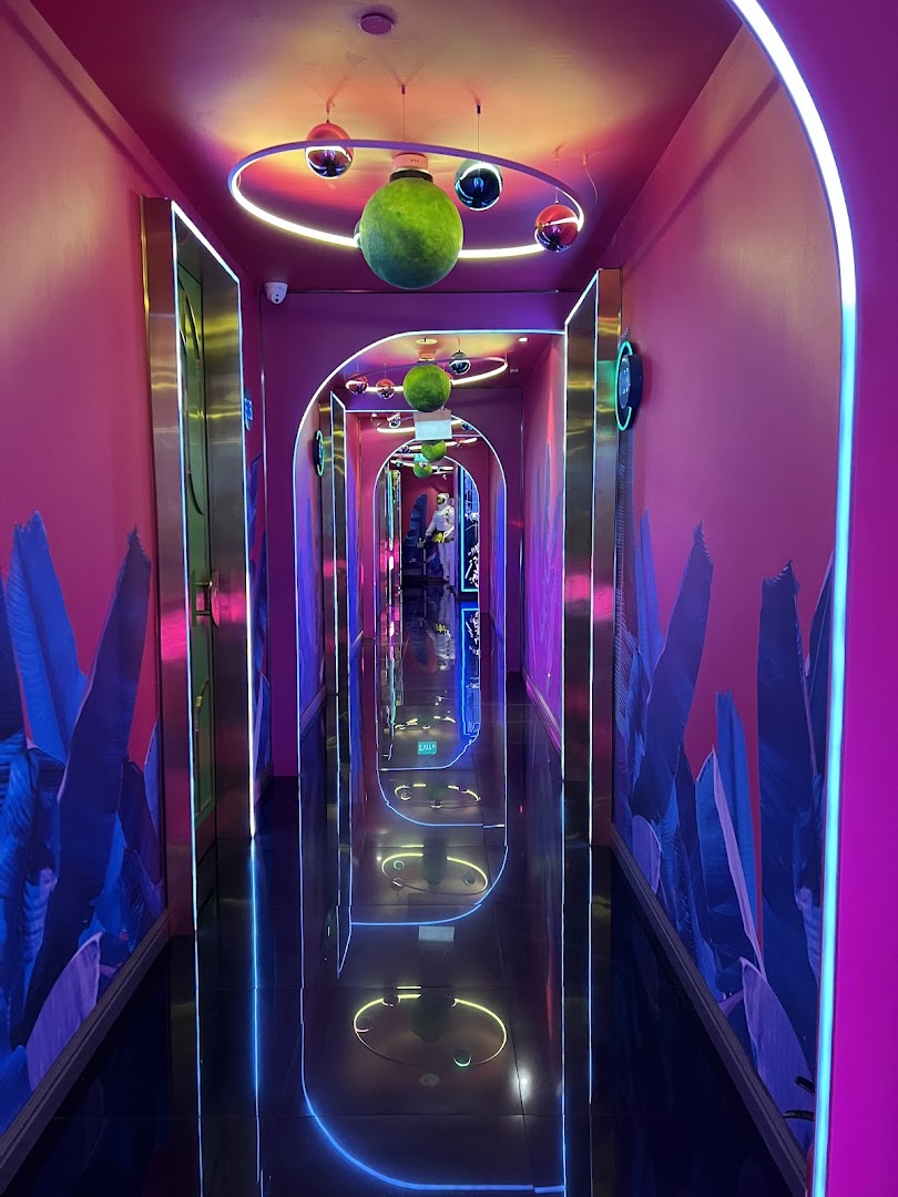 A vibrant, neon-lit hallway with reflective floors leading to KTV rooms.
