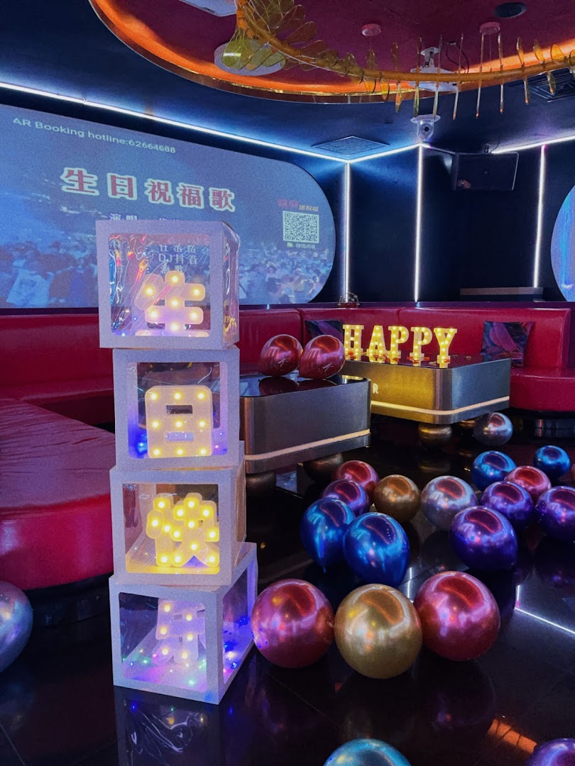 Vibrant KTV room decorated for a celebration with illuminated signs and balloons.