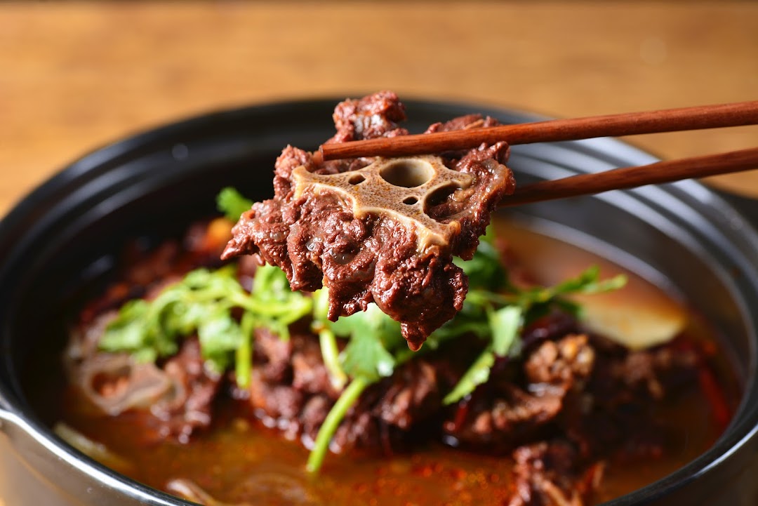 Chopsticks lifting a piece of braised oxtail from a rich, savory stew in a black pot.