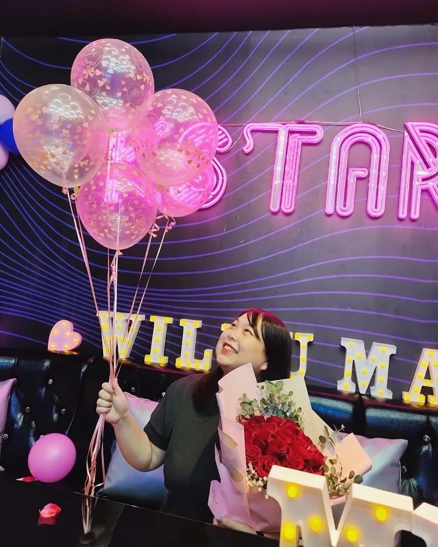 A person celebrating with balloons and a bouquet in a vibrant K.STAR KTV room.