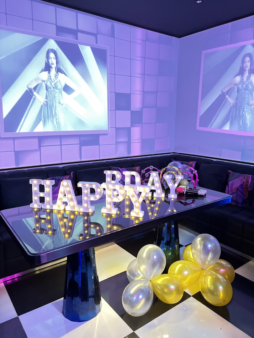 A vibrant KTV room with 'HAPPY BDAY' lights, balloons, and large screens displaying visuals.