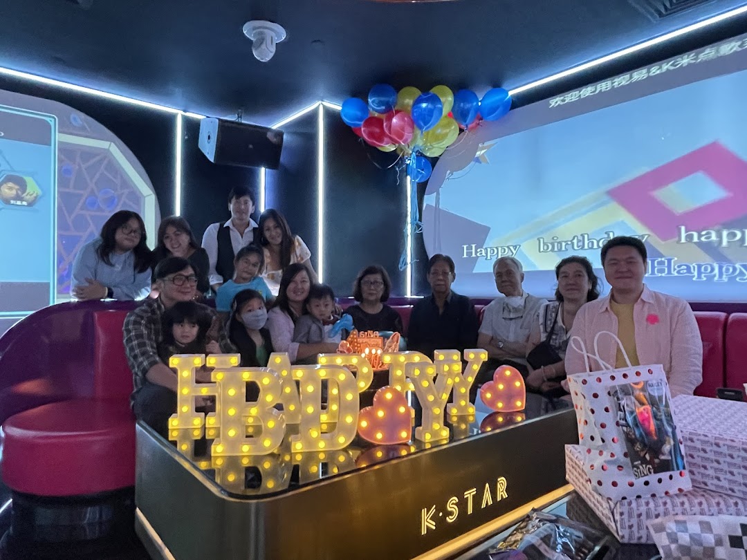 A group celebrates a birthday with balloons and a 'Happy Birthday' sign in a KTV room.