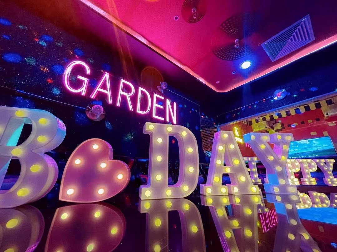 Vibrant KTV room interior with illuminated 'BIRTHDAY' letters and a 'GARDEN' neon sign.