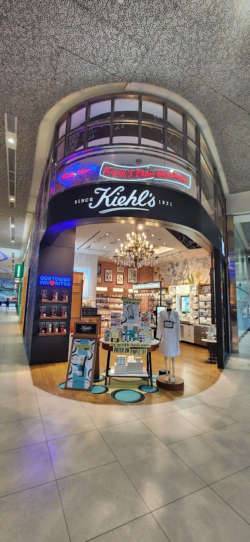 The brightly lit entrance of Kiehl's skincare store, featuring neon signs and product displays.