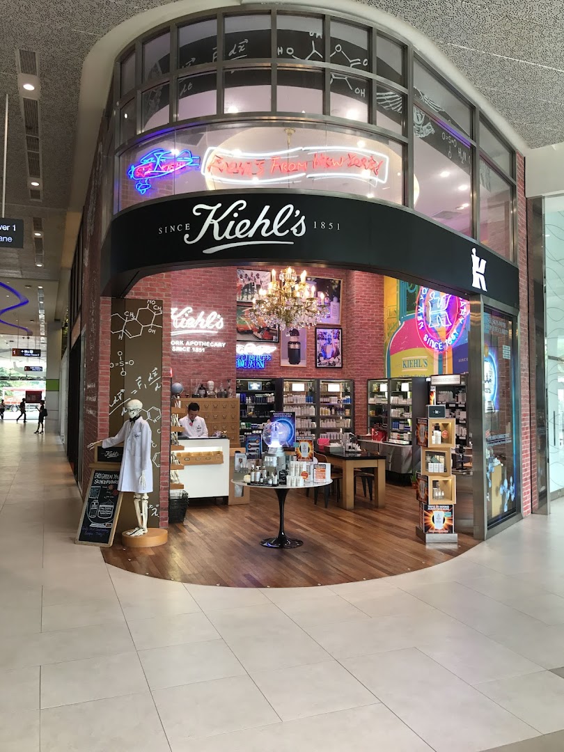 The Kiehl's shop front features a skeleton mascot, neon signs, and a brick wall interior, inviting customers in.