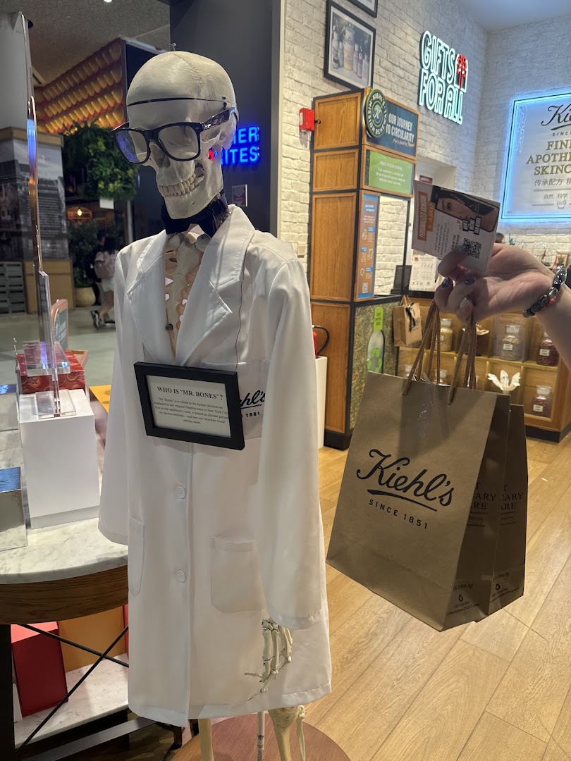 Kiehl's iconic 'Mr. Bones' skeleton display in a lab coat, with a customer's shopping bag inside the store.