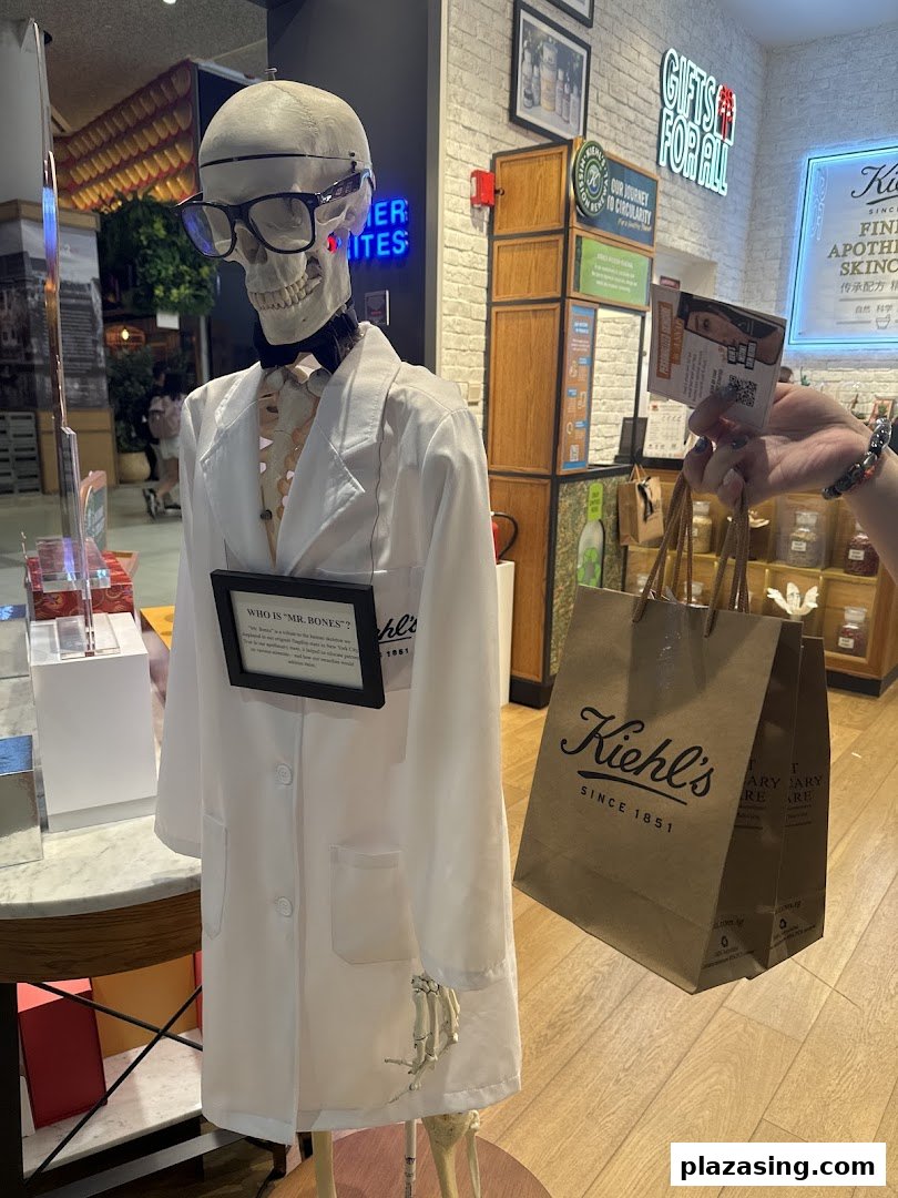 Kiehl's iconic 'Mr. Bones' skeleton display in a lab coat, with a customer's shopping bag inside the store.