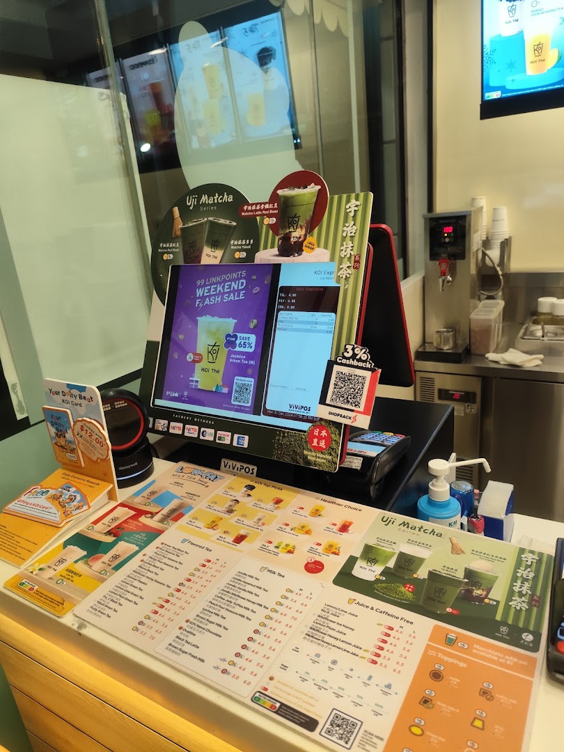 A vibrant counter at KOI Thé, showcasing various bubble tea menus, promotional displays, and payment options.