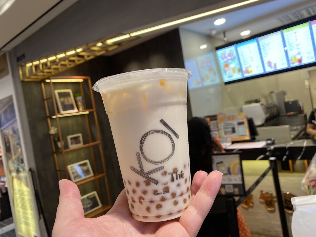 A hand holds a refreshing bubble tea from KOI Thé, showcasing the popular drink and shop interior.