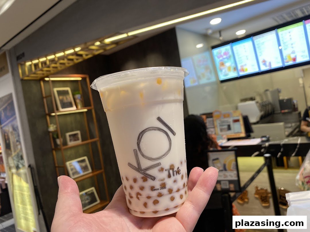A hand holds a refreshing bubble tea from KOI Thé, showcasing the popular drink and shop interior.