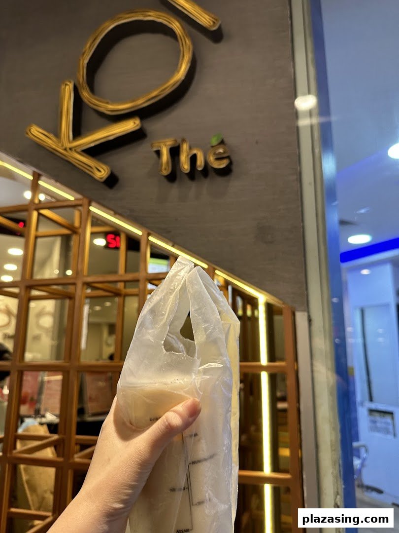 A hand holds a bubble tea drink in front of the KOI Thé shop sign.