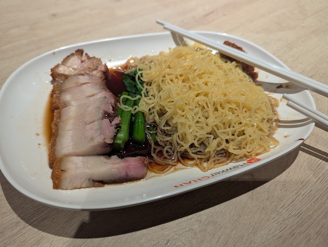 A delicious plate of roasted pork belly with noodles and greens, served with chopsticks.