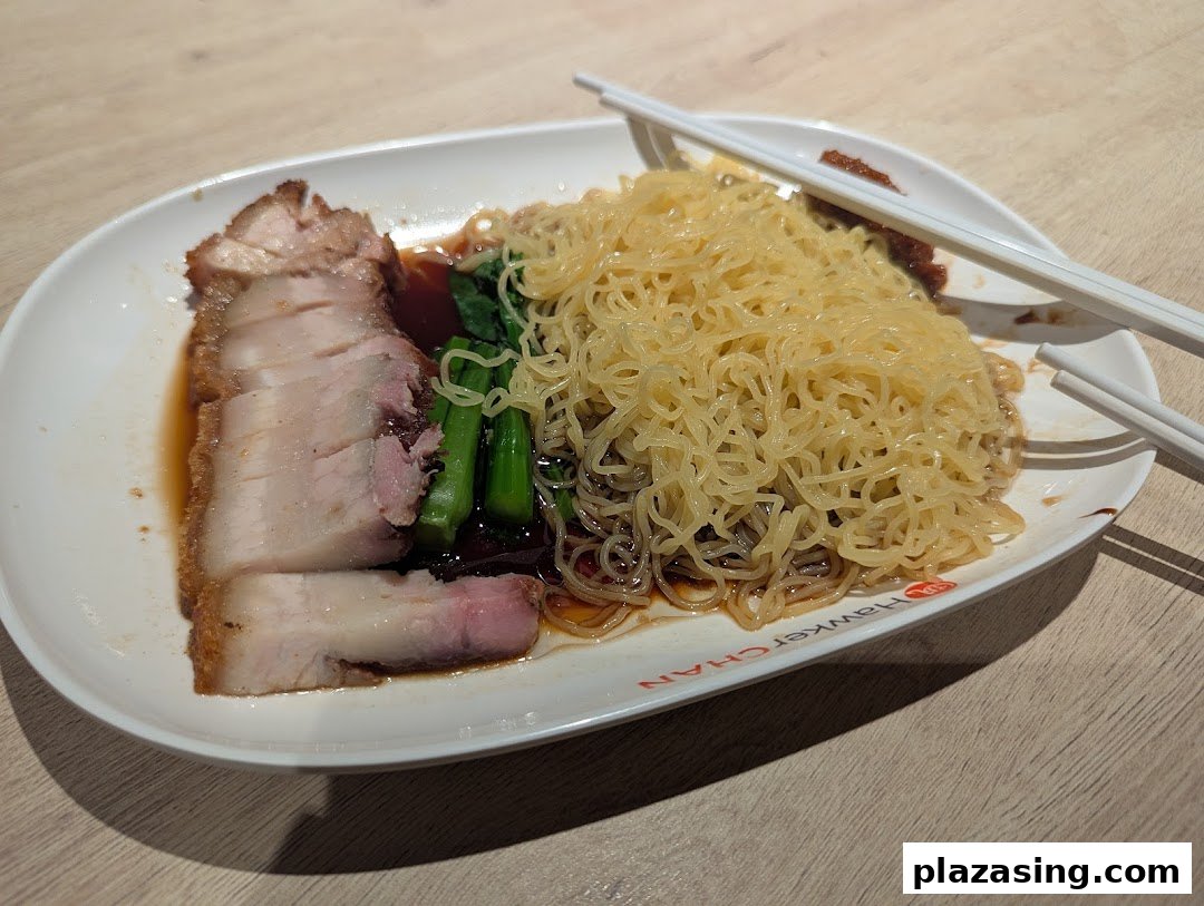 A delicious plate of roasted pork belly with noodles and greens, served with chopsticks.