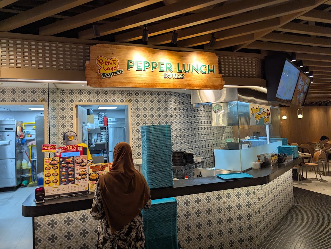 A customer orders at the Pepper Lunch Express counter within a bustling food hall.