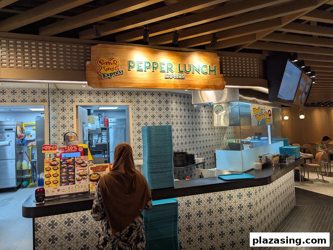 A customer orders at the Pepper Lunch Express counter within a bustling food hall.