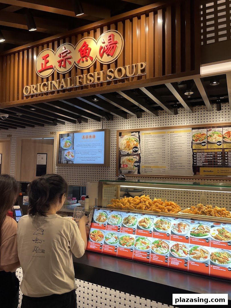 Customers at Original Fish Soup stall in Kopitiam Food Hall, featuring menu boards and food displays.