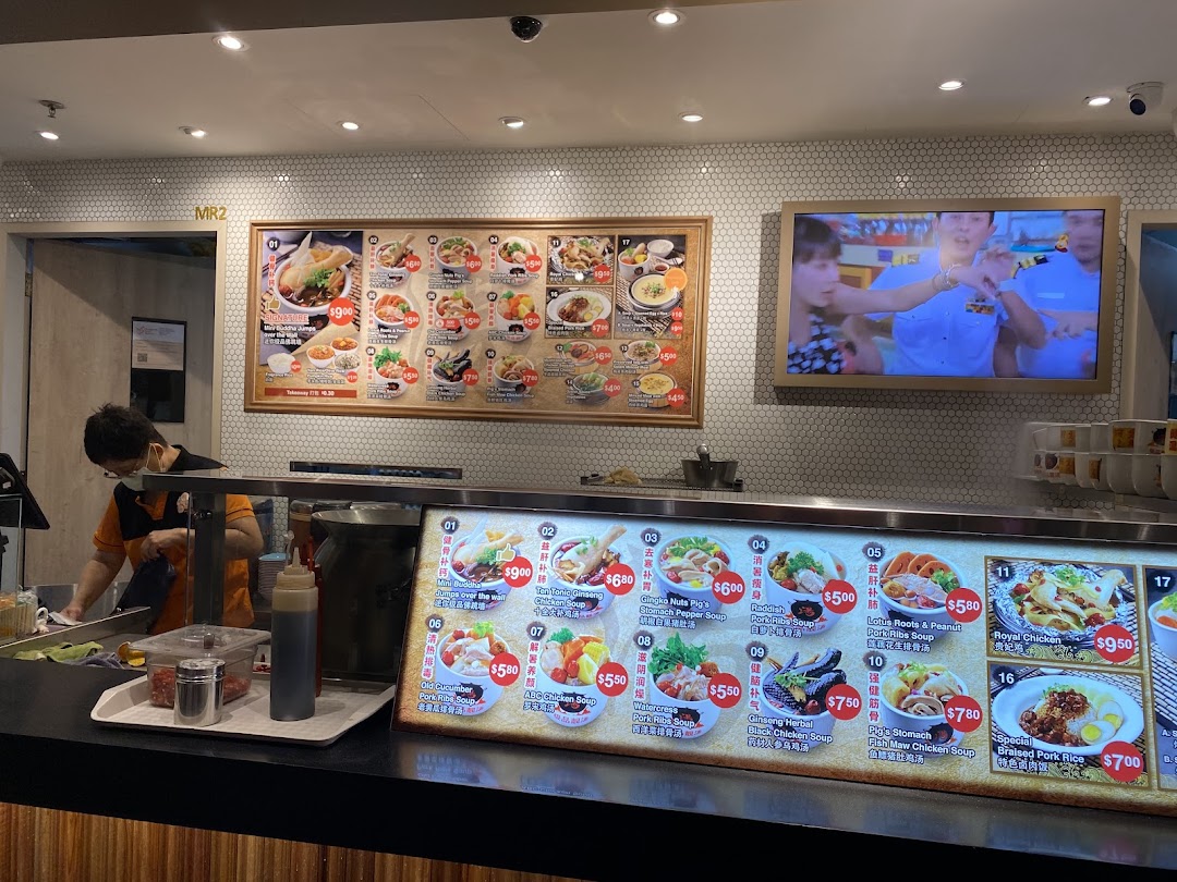 An interior view of a food stall counter with large menu displays and a staff member preparing food.