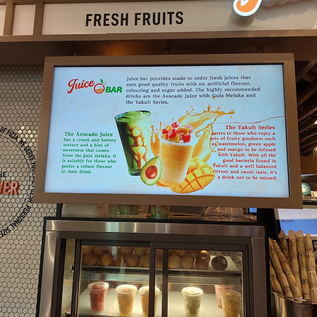 A vibrant display board promoting fresh juices, including avocado and Yakult series, above a refrigerated drink display.