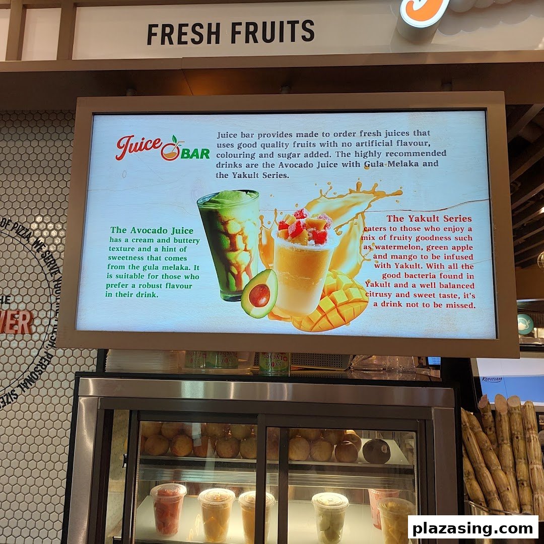 A vibrant display board promoting fresh juices, including avocado and Yakult series, above a refrigerated drink display.