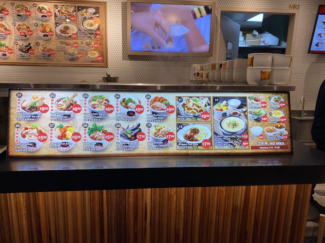 A brightly lit food stall counter displaying detailed menu boards with various soup and rice dishes.