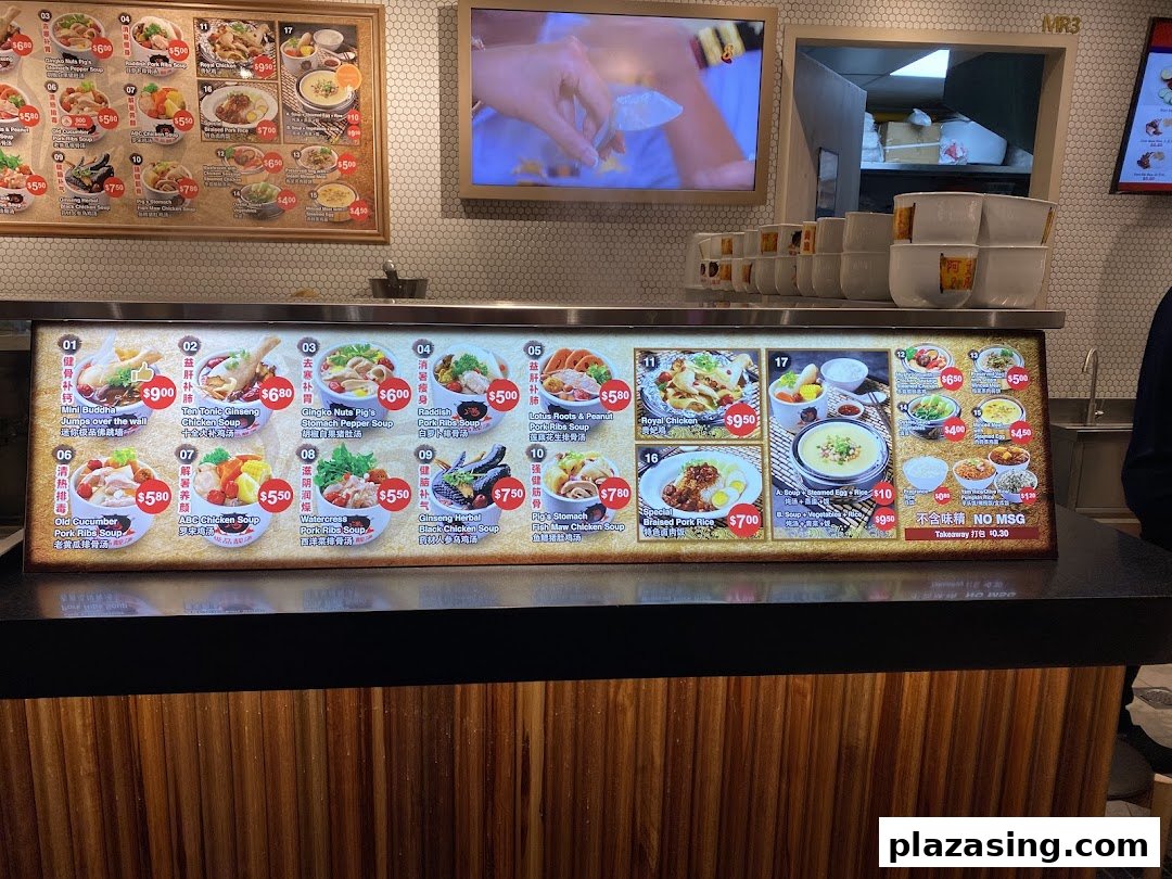 A brightly lit food stall counter displaying detailed menu boards with various soup and rice dishes.