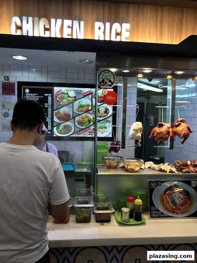A customer at a Chicken Rice stall in Kopitiam Food Hall, featuring hanging roasted chickens and a digital menu.