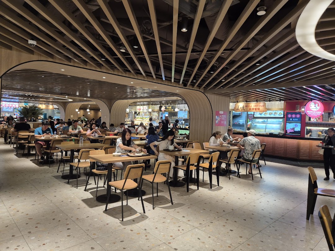 A bustling food hall interior with numerous diners enjoying meals at various food stalls.