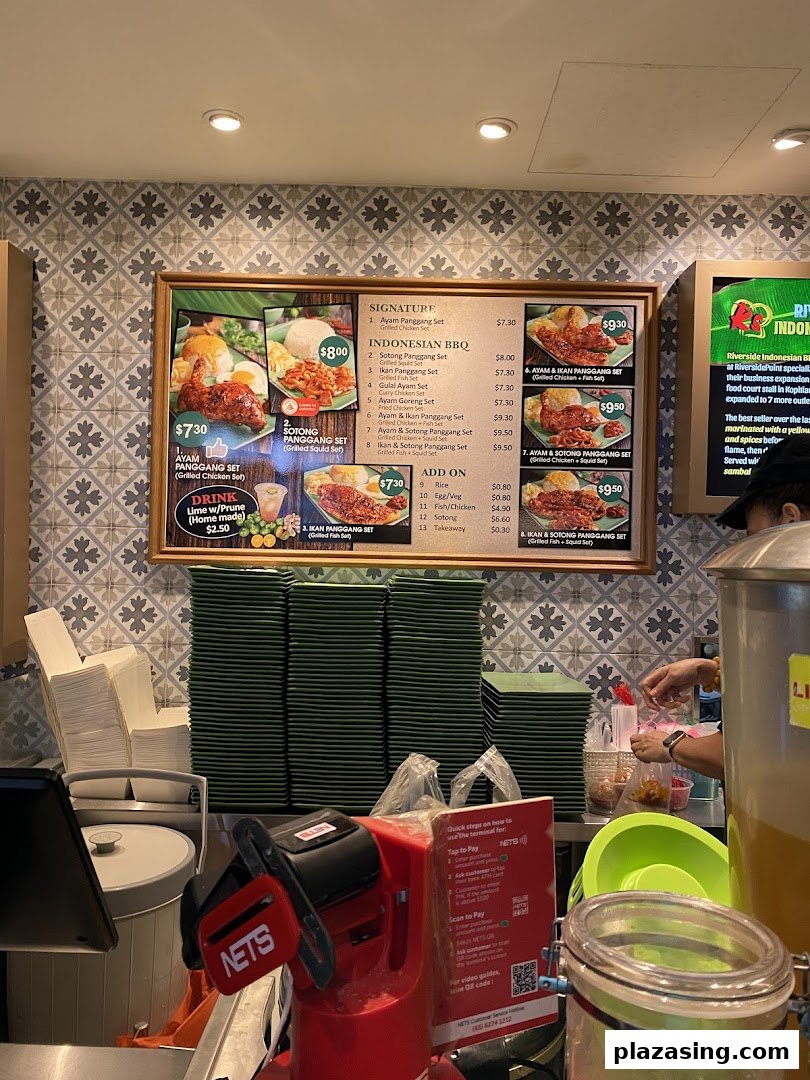 A menu board displaying Indonesian BBQ dishes and prices at a food hall counter.