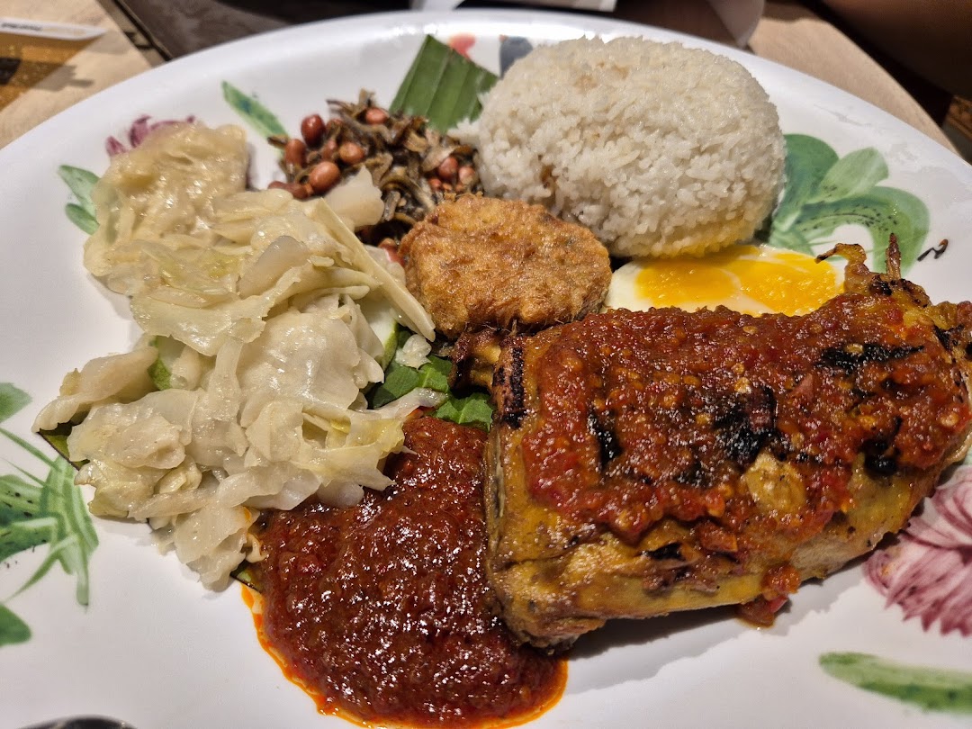A vibrant plate of Nasi Lemak featuring spicy fried chicken, fluffy rice, egg, and traditional accompaniments.