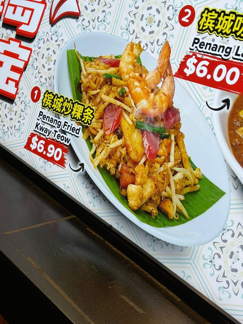 Close-up of a menu board displaying Penang Fried Kway Teow and Penang Laksa with prices.