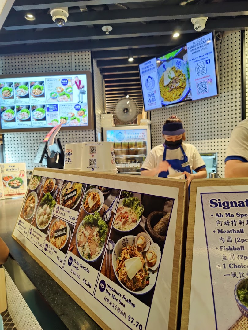 An interior view of Kopitiam Food Hall, featuring a food stall counter with menu displays and a staff member.